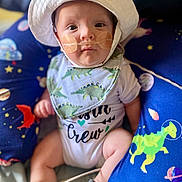 Calix joined the competition — help win amazing prizes! baby, infant, hat, bib, nasal_cannula, green_socks, dinosaur_pattern, space_theme, cushion, blue_background, white_clothing, close_up, indoors, seated, footwear, cute, child, portrait, medical_device, expression