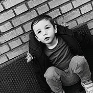 Kelyan participe au concours pour gagner de l'argent avec cette photo : child, toddler, boy, brick_wall, bench, sneakers, jacket, coat, black_and_white, portrait, sitting, casual_clothing, short_hair, expression, eyes, face, outdoor, texture, candid, seat
