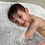 child, bathtub, bubbles, foam, water, wet_hair, smile, happy, portrait, indoor, skin, head, ear, eye, cheeks, arm, bath_time, playful, soap, toddler