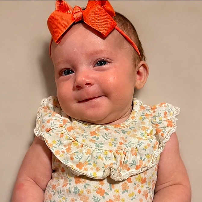 Anastasia joined the competition — help win amazing prizes! baby, child, headband, bow, orange, floral_dress, smile, portrait, cute, infant, skin, face, young, adorable, innocence, person, baby_girl, background, clothing, expression
