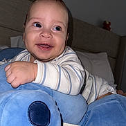Milán is registered to the contest to win money with this photo: baby, infant, child, smiling, portrait, indoors, bedroom, bed, bedding, stuffed_toy, plush_toy, blue, striped_clothing, long_sleeves, sitting, lying_down, face, happy, close_up, photography