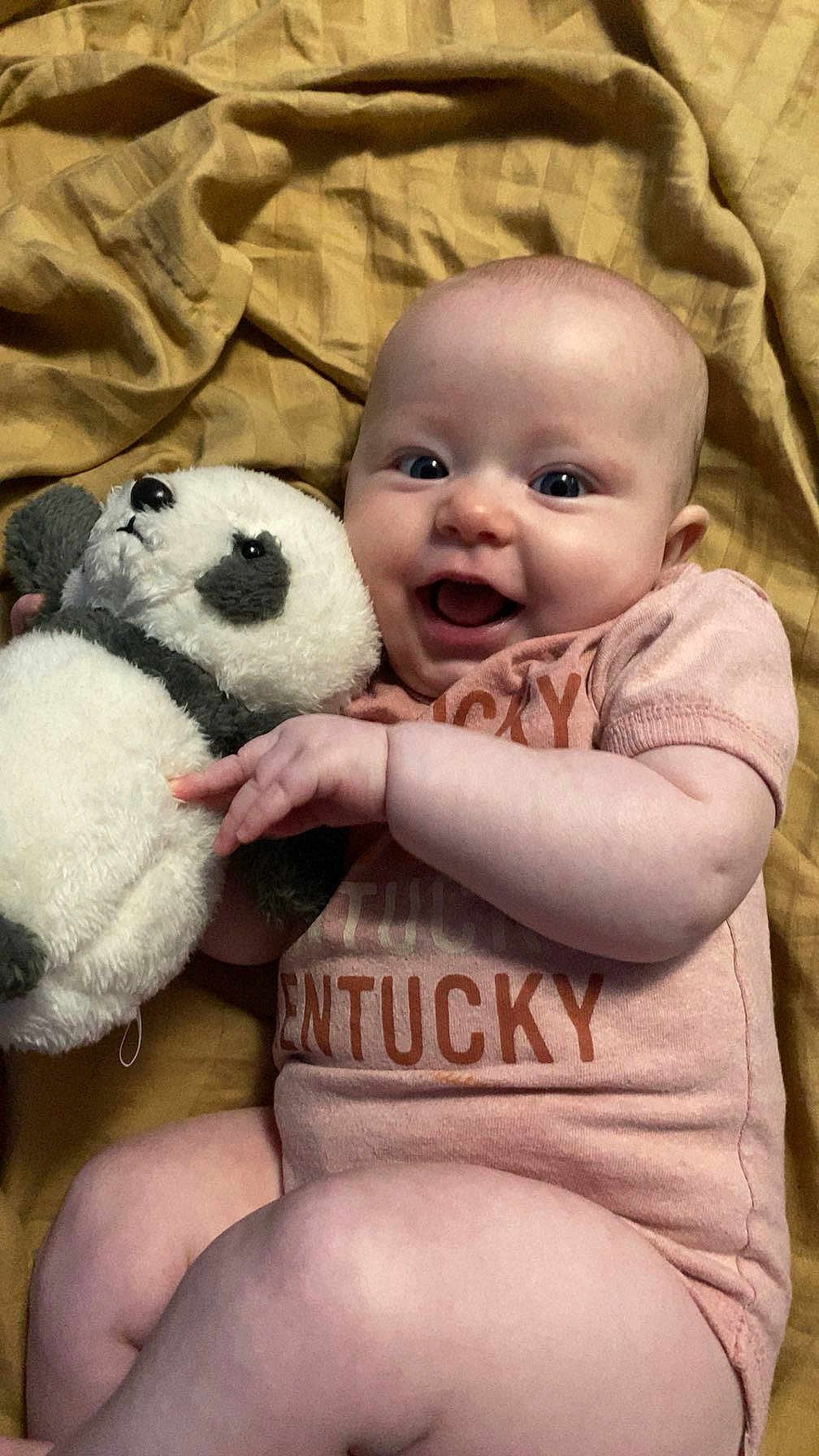 Enora joined the competition — help win amazing prizes! baby, infant, smiling, stuffed_animal, panda, blanket, onesie, clothing, happy, cute, lying_down, child, toy, face, person, skin, hand, furniture, indoors, soft_toy