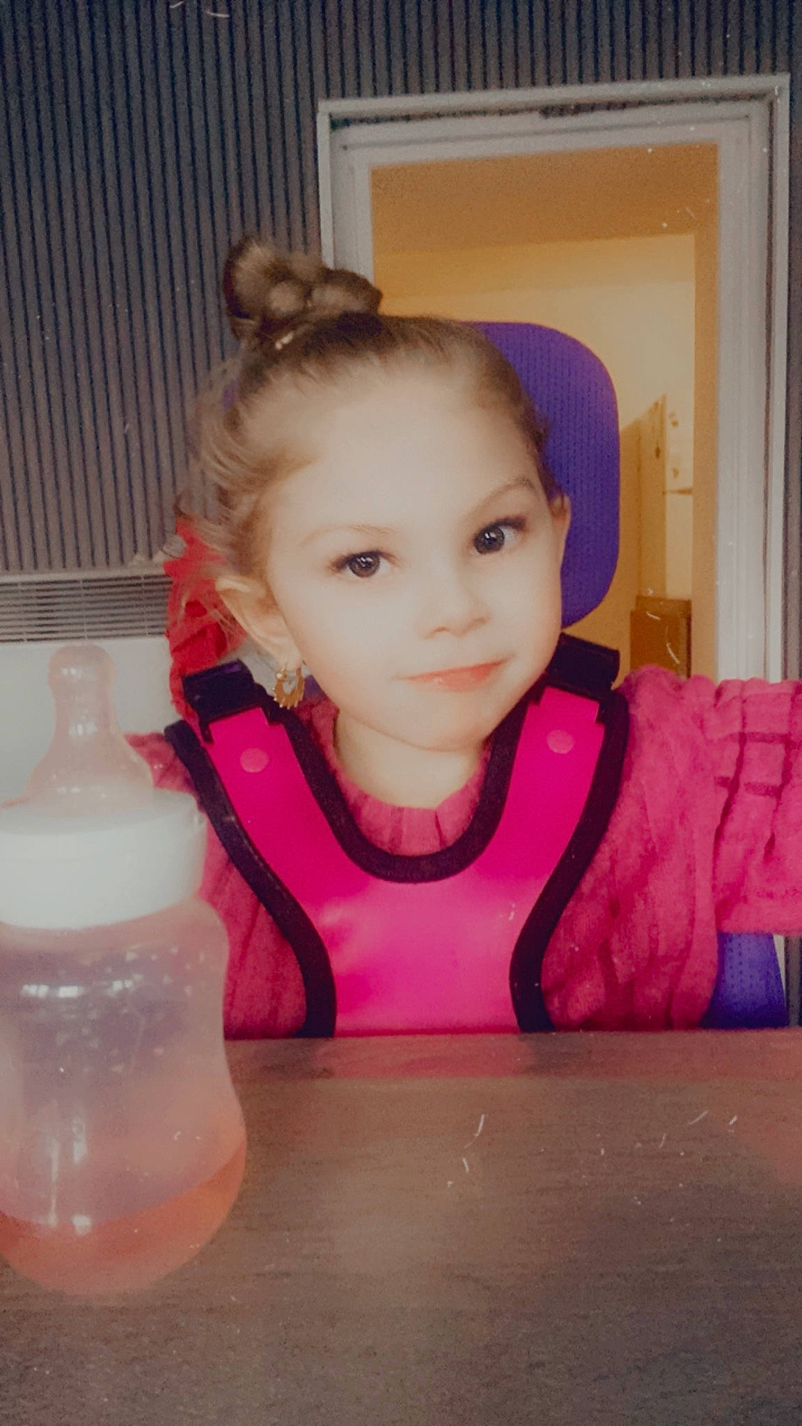 Inaya participe au concours pour gagner de l'argent avec cette photo : baby_toddler_clothing, chair, cheek, child, drinkware, eyebrow, eyelash, face, fashion_accessory, fun, hair_tie, happy, magenta, person, pink, plastic_bottle, purple, sitting, skin, sleeve