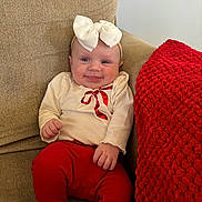 Anna is registered to the contest to win money with this photo: baby, smiling, child, bow, headband, red_pants, cream_top, ribbon, knitted_blanket, chair, beige, textured, happy, cute, indoors, infant, portrait, sitting, cozy, clothing