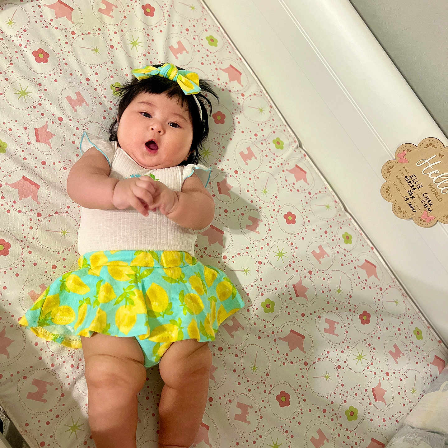 Ellie joined the competition — help win amazing prizes! baby, infant, crib, mattress, lying_down, portrait, face, smiling, open_mouth, bow, hair, dress, skirt, lemon_pattern, colorful_clothing, nursery, patterned_blanket, indoor, crib_rail, cute