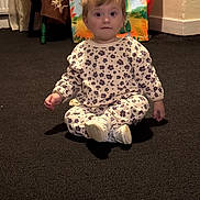 Elizabeth joined the competition — help win amazing prizes! toddler, child, pajamas, floral_pattern, sitting, carpet, indoor, gift_bags, balloon, celebration, curtains, table, floor, wall, expression, person, young_child, cute, clothing, portrait