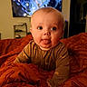 baby, tongue_out, blanket, orange, cute, indoor, child, face, expression, infant, cozy, bedroom, television, sleepwear, person, smiling, young, warm_lighting, home, funny_face