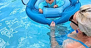 Oliver is registered to the contest to win money with this photo: baby, child, swimming_pool, water, float, inflatable, helmet, adult, woman, sunglasses, sunshade, blue, summer, fun, outdoor, safety, care, person, swimwear, happy