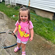 Denver is registered to the contest to win money with this photo: child, toddler, pink_shirt, tweety_bird, hose, water, blue_tongue, shorts, sandals, outdoor, grass, concrete, playful, happy, summer, person, fun, garden, casual_clothing, daytime
