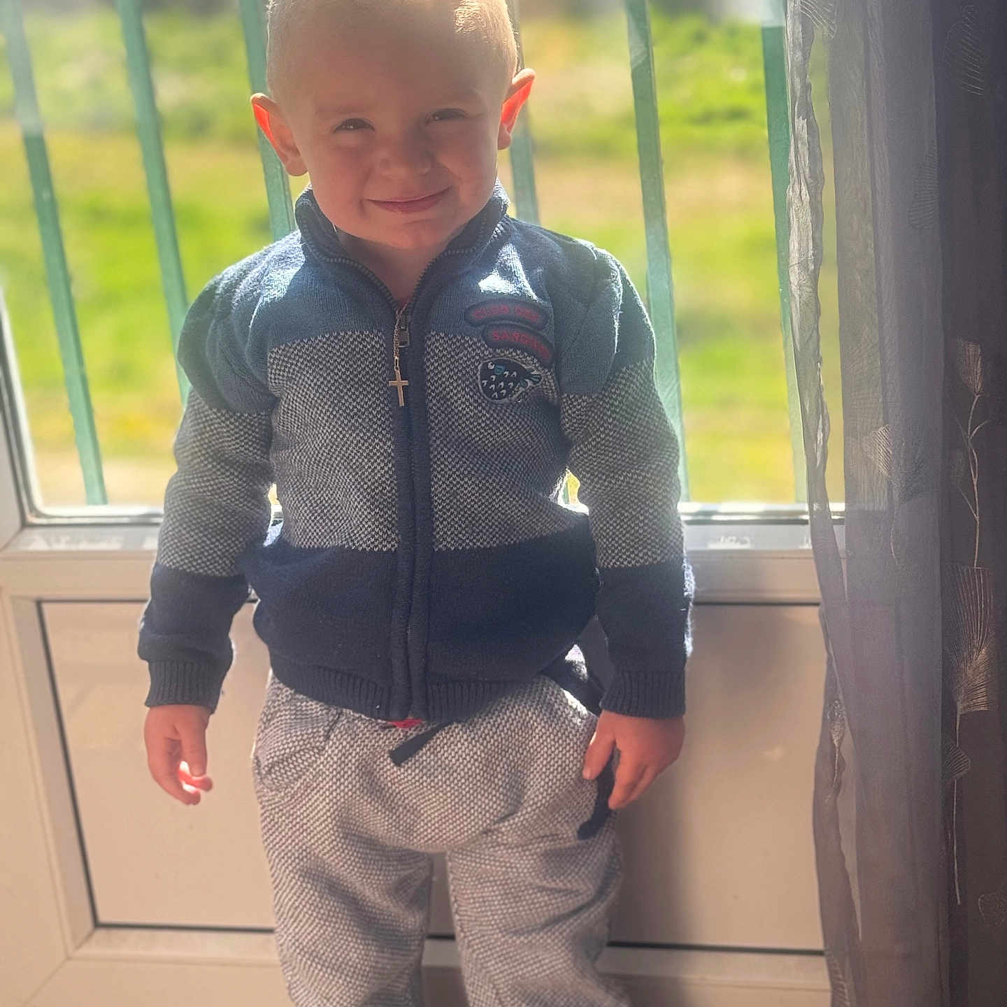 Alezio a rejoint le concours — aidez-le/la à gagner de superbes lots ! boy, bright, casual, child, clothing, cross_necklace, curtain, cute, floor, hands, happy, indoor, pants, portrait, smiling, standing, sunlight, sweater, window, young