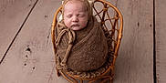 Alfie is registered to the contest to win money with this photo: baby, newborn, sleeping, wrapped, blanket, bonnet, wicker_chair, wooden_floor, cozy, cute, infant, portrait, indoors, peaceful, tied_bow, knit, small_chair, child, soft_texture, resting