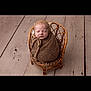 baby, newborn, sleeping, wrapped, blanket, bonnet, wicker_chair, wooden_floor, cozy, cute, infant, portrait, indoors, peaceful, tied_bow, knit, small_chair, child, soft_texture, resting