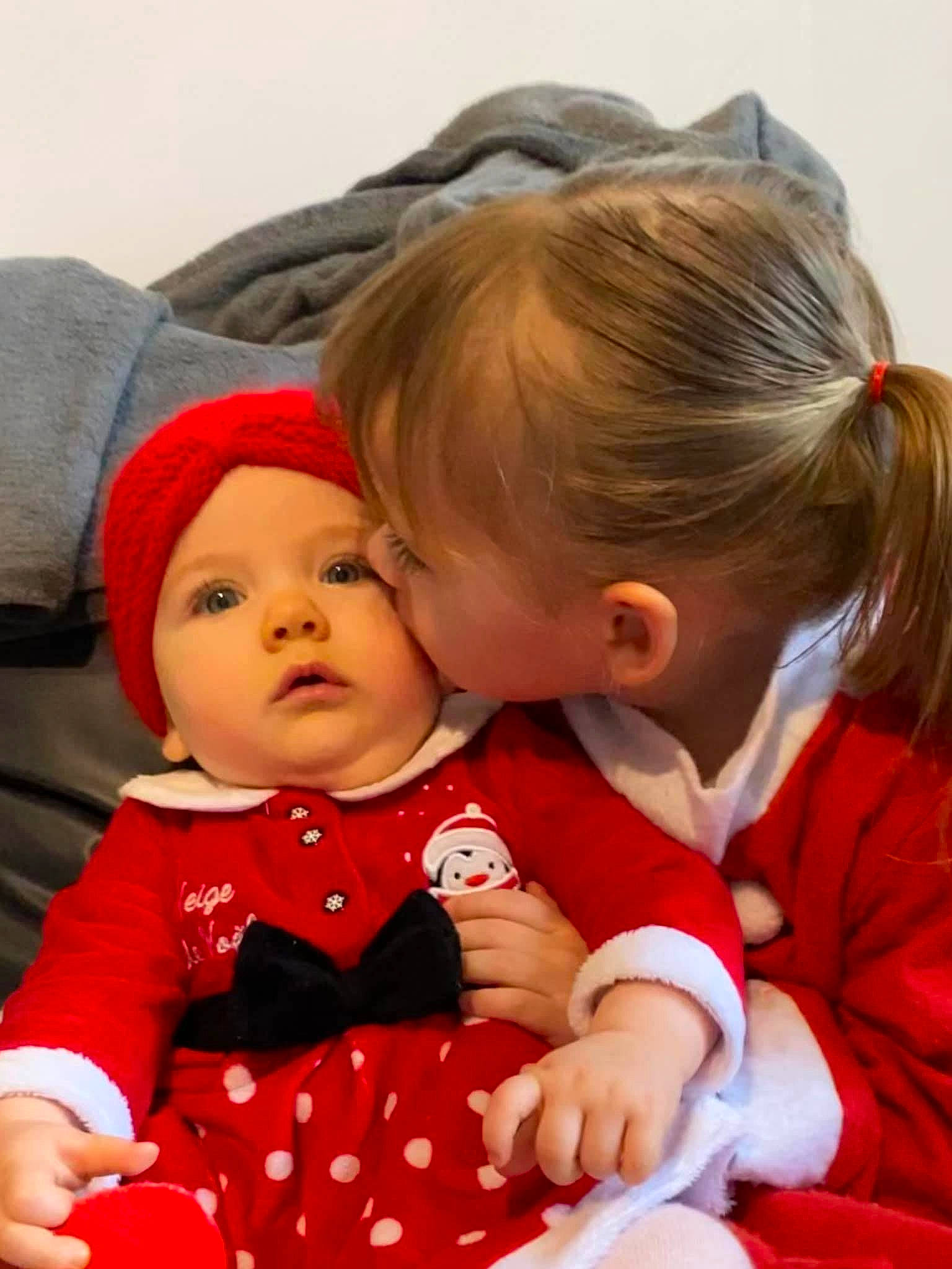 Mila Et Lya a rejoint le concours — aidez-le/la à gagner de superbes lots ! baby, baby_toddler_clothing, carmine, cheek, child, christmas, christmas_eve, comfort, dress, face, fun, gesture, happy, headwear, holiday, lap, pattern, person, sitting, skin