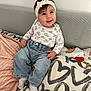 baby, child, headband, jeans, socks, blanket, couch, pillow, heart_pattern, smiling, indoor, cute, happy, clothing, portrait, infant, home, soft, seated, cozy