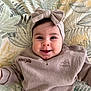 baby, smiling, headband, bow, sweater, infant, face, child, portrait, happy, lying_down, blanket, patterned, cozy, cute, indoors, clothing, closeup, person, expression