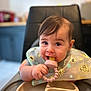 baby, bib, child, cute, face, feeding, food, hand, happy, high_chair, indoor, infant, kitchen, person, playful, portrait, smiling, table, teething_toy, young_child