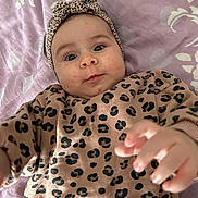 Mira participe au concours pour gagner de l'argent avec cette photo : baby, infant, leopard_print, headband, clothing, hand, face, blanket, pattern, purple, cute, portrait, child, lying_down, expression, skin, person, young, indoor, candid