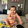 baby, smiling, sitting, bed, towel, hand, face, indoor, room, furniture, lamp, painting, hairclip, skin, clothing, foot, toy, black_object, happy, child