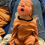Malachi joined the competition — help win amazing prizes! baby, sleeping, infant, onesie, orange_clothing, person, lap, jeans, ripped_jeans, blanket, fabric, indoor, resting, young_child, soft_texture, cozy, cute, peaceful, head, mouth_open