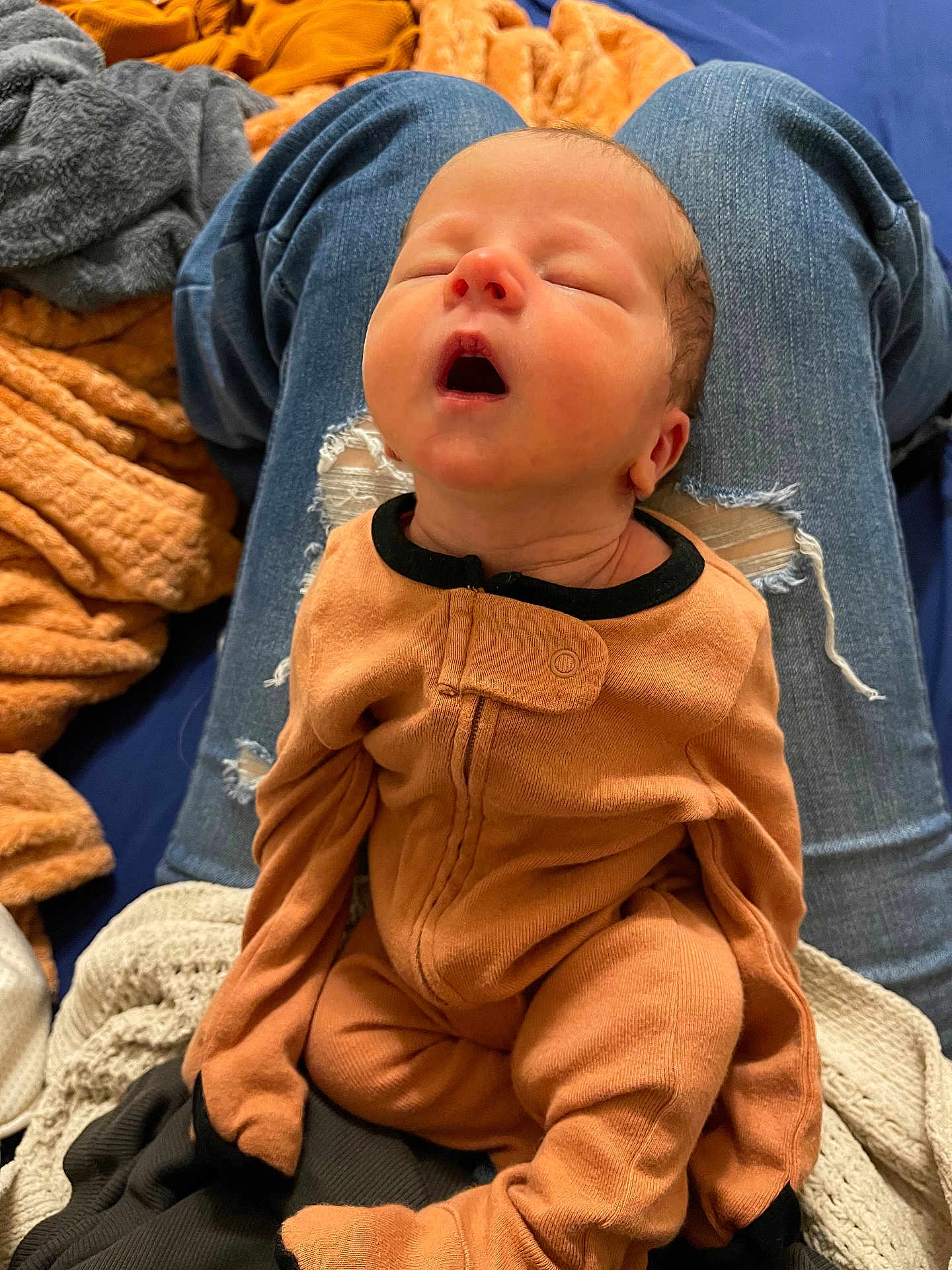 Malachi joined the competition — help win amazing prizes! baby, sleeping, infant, onesie, orange_clothing, person, lap, jeans, ripped_jeans, blanket, fabric, indoor, resting, young_child, soft_texture, cozy, cute, peaceful, head, mouth_open