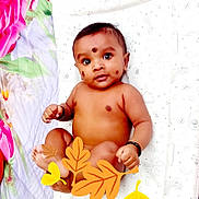 Vishakan joined the competition — help win amazing prizes! baby, infant, face, skin, lying_down, decorative_marks, bracelet, hand, foot, expression, patterned_sheet, floral_fabric, leaf_stickers, cute, child, indoors, colorful, smiling, person, adorable