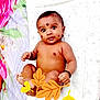 baby, infant, face, skin, lying_down, decorative_marks, bracelet, hand, foot, expression, patterned_sheet, floral_fabric, leaf_stickers, cute, child, indoors, colorful, smiling, person, adorable