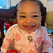 Zennayah joined the competition — help win amazing prizes! baby, smiling, child, high_chair, pink_bow, curly_hair, onesie, ladybug_pattern, red_cup, indoors, furniture, person, happy, cute, toddler, home, seat, clothing, face, portrait
