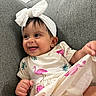 baby, child, smiling, headband, bow, flamingo_print, dress, couch, grey, happy, cute, infant, clothing, playful, person, portrait, indoors, fabric, hand, sitting