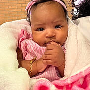 Aubree joined the competition — help win amazing prizes! baby, infant, pink_headband, pink_clothing, blanket, white_blanket, pink_blanket, bracelet, hand, face, curly_hair, indoors, brick_wall, person, cute, cozy, portrait, closeup, child, soft_texture