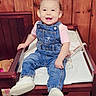 toddler, child, smiling, denim_overalls, pink_bows, white_shoes, changing_table, wooden_wall, indoor, baby, cute, happy, sitting, person, furniture, face, young_child, hair_bows, footwear, apparel