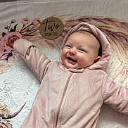 Kinsley is registered to the contest to win money with this photo: baby, infant, pink_onesie, smiling, face, blanket, floral_pattern, wooden_sign, two_months, cute, happy, lying_down, soft_texture, child, person, hooded_clothing, indoors, portrait, young_child, cozy