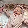 baby, infant, pink_onesie, smiling, face, blanket, floral_pattern, wooden_sign, two_months, cute, happy, lying_down, soft_texture, child, person, hooded_clothing, indoors, portrait, young_child, cozy