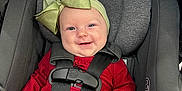 Kinsley is registered to the contest to win money with this photo: baby, car_seat, graco, smile, red_clothing, headband, green_bow, harness, infant, child, safety, seatbelt, cute, portrait, indoor, person, happy, clothing, seat, baby_fashion
