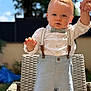 toddler, child, boy, face, outdoor, sunlight, clothing, shirt, bow_tie, suspenders, shorts, wicker_chair, hand_holding, portrait, cute, person, expression, hair, standing, garden