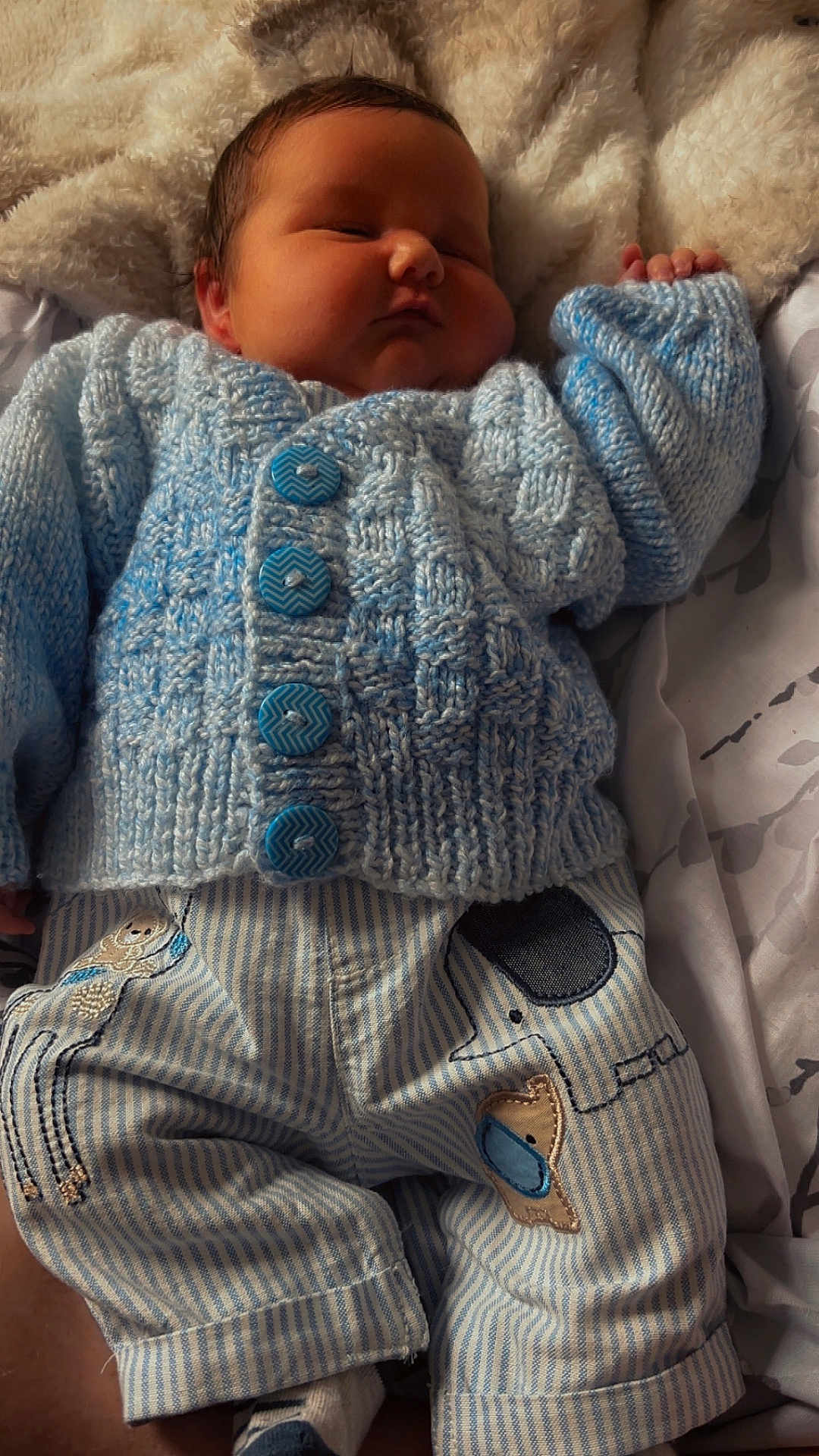 George-Thomas is registered to the contest to win money with this photo: baby, sleeping, blue_sweater, knitted, striped_pants, patches, blanket, cozy, infant, cute, child, soft_lighting, resting, hand, fabric, textile, portrait, indoors, peaceful, newborn