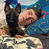 dog, puppy, person, bed, blanket, pillow, indoor, lying_down, cuddle, pet, animal, young_adult, casual, resting, comfort, domestic, face, ears, looking_at_camera, relaxation