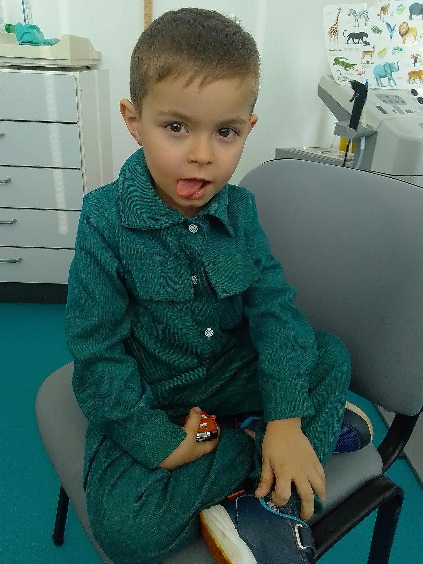 Antonio participe au concours pour gagner de l'argent avec cette photo : child, boy, toy_car, chair, clothing, footwear, tongue_out, playful, indoor, medical_equipment, poster, animal_poster, furniture, person, sitting, casual, young_child, hair, face, expression