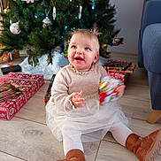 Anna participe au concours pour gagner de l'argent avec cette photo : child, toddler, baby, christmas_tree, christmas_presents, gift, ornament, holiday, living_room, sitting, smile, happy, dress, tutu, boots, stockings, wood_floor, tree_skirt, wrapped_gift, decorations