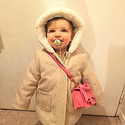 Anna participe au concours pour gagner de l'argent avec cette photo : accessory, beige_coat, blue_eyes, candid, carpet_floor, child, coat, fashion, hood, indoor, pacifier, pacifier_clip, pink_purse, playful, portrait, shoes, smile, standing, toddler, wall_background