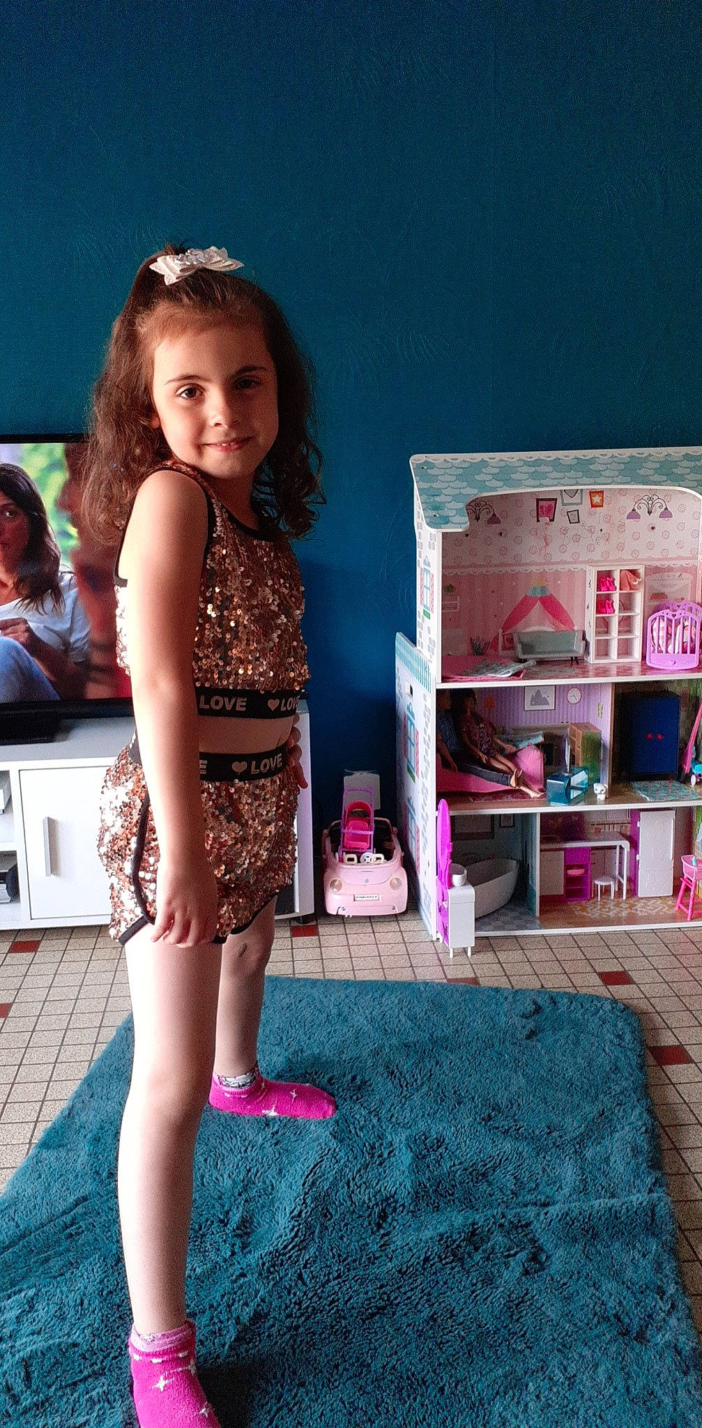 Myla participe au concours pour gagner de l'argent avec cette photo : carpet, child, event, fashion_design, flooring, fun, happy, human_leg, joy, knee, leisure, magenta, person, pink, play, room, sandal, shelf, sitting, smile