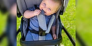 Arthur joined the competition — help win amazing prizes! baby, stroller, blue_eyes, child, outdoor, grass, playful, smile, seatbelt, clothing, infant, cute, happy, person, summer, seat, chewing, young_child, daylight, casual