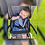 baby, stroller, blue_eyes, child, outdoor, grass, playful, smile, seatbelt, clothing, infant, cute, happy, person, summer, seat, chewing, young_child, daylight, casual