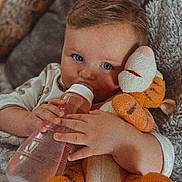 Arthur is registered to the contest to win money with this photo: baby, bottle, plush_toy, tiger, tattoo, child, couch, blanket, blue_eyes, cute, indoor, person, soft_toy, snuggling, hand, infant, relaxing, cozy, portrait, young_child