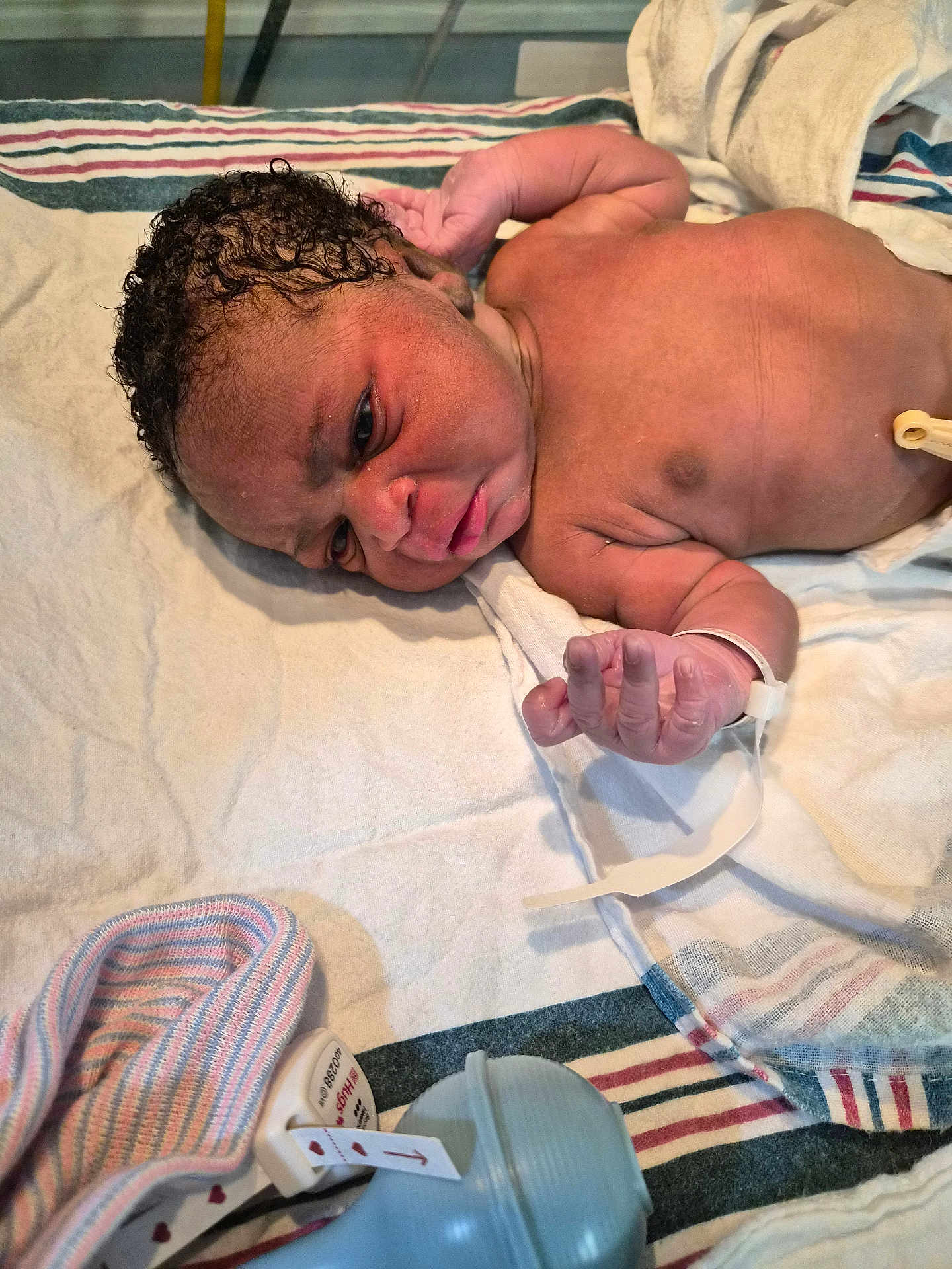 Meilani joined the competition — help win amazing prizes! newborn, baby, hospital, blanket, infant, face, skin, arm, hand, hospital_id_bracelet, curly_hair, lying_down, striped_blanket, medical, baby_hat, closeup, person, newborn_care, indoors, patient