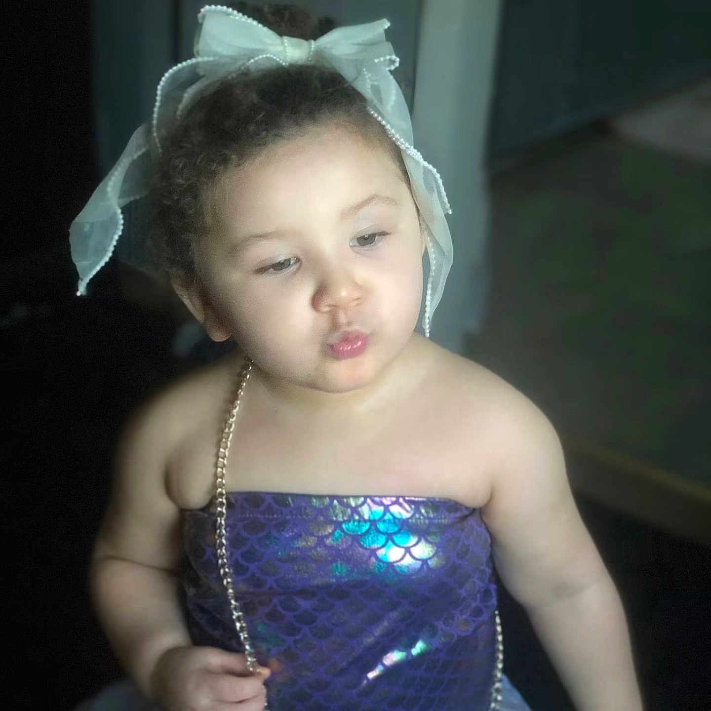 Zara is registered to the contest to win money with this photo: toddler, child, girl, curly_hair, bow, mermaid_outfit, purple_dress, shiny_clothing, necklace, puckered_lips, indoor, cute, portrait, baby, fashion, costume, playful, young_child, person, headwear