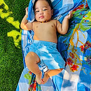 Djewen a rejoint le concours — aidez-le/la à gagner de superbes lots ! baby, child, grass, blanket, blue_shorts, necklace, outdoor, sunlight, patterned_blanket, greenery, relaxing, infant, skin, bare_chest, colorful, nature, cute, summer, lying_down, peaceful