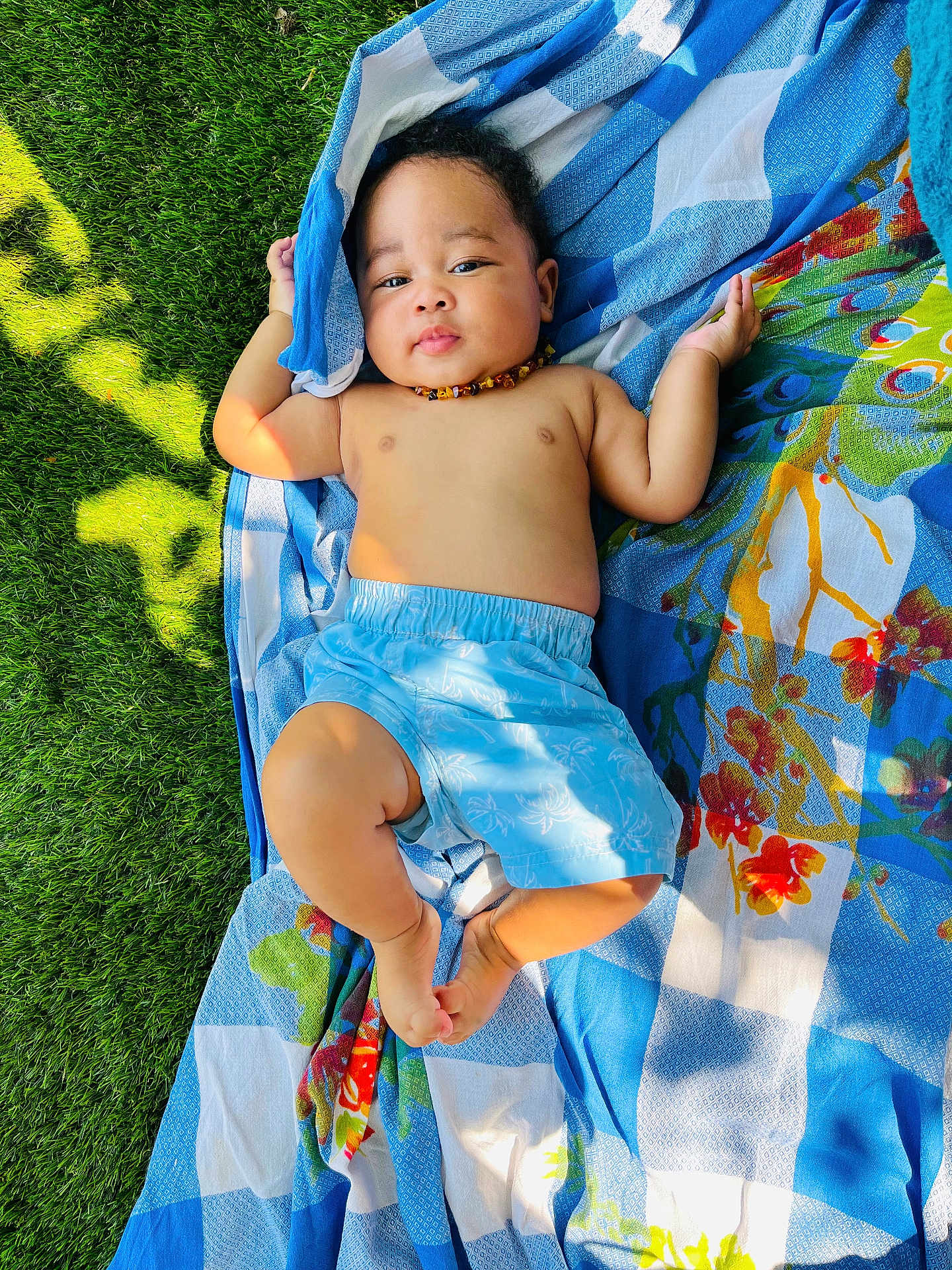 Djewen a rejoint le concours — aidez-le/la à gagner de superbes lots ! baby, child, grass, blanket, blue_shorts, necklace, outdoor, sunlight, patterned_blanket, greenery, relaxing, infant, skin, bare_chest, colorful, nature, cute, summer, lying_down, peaceful