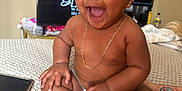Genesis is registered to the contest to win money with this photo: baby, smiling, laughing, sitting, diaper, gold_chain, indoor, bedspread, smartphone, tattoo, arm, person, child, cute, happy, skin, hair, face, expression, furniture