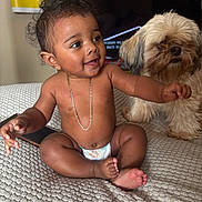 Genesis is registered to the contest to win money with this photo: baby, child, diaper, gold_chain, curly_hair, dog, pet, bedspread, indoor, furniture, smiling, happy, cute, skin, person, animal, companion, home, friendship, texture