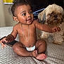 baby, child, diaper, gold_chain, curly_hair, dog, pet, bedspread, indoor, furniture, smiling, happy, cute, skin, person, animal, companion, home, friendship, texture